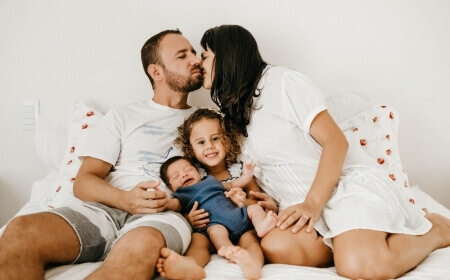 Familienleben: Familie, die gemeinsam auf dem Bett sitzt.