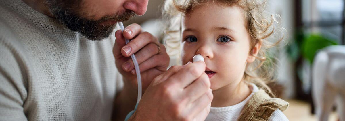 Papa, der seiner Tochter mit einem manuellen Nasensauger die Nase reinigt.