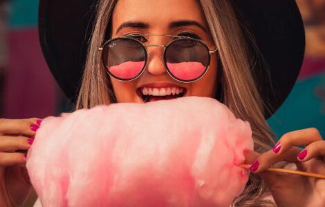 Frau mit einer Sonnenbrille, die rosafarbene Zuckerwatte isst.