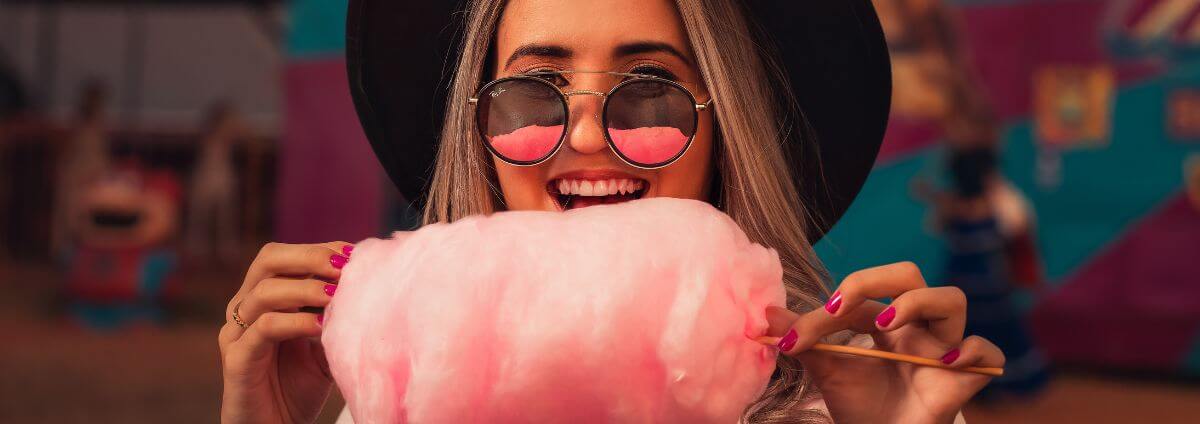 Frau mit einer Sonnenbrille, die rosafarbene Zuckerwatte isst.