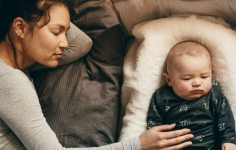 Baby, das in einem Beistellbett neben dem Bett seiner Mama liegt.